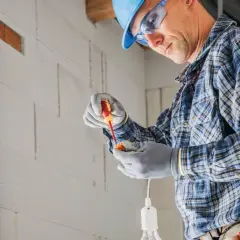 Elektryk w kasku i okularach montuje oprawkę żarówki. Cena za punkt elektryczny zależy od złożoności instalacji.