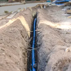 Niebieski kabel w wykopie, zabezpieczony w peszlu, czeka na zasypanie.