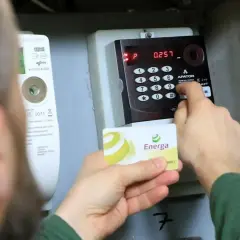 Osoba dokonuje doładowanie licznika przedpłatowego, wprowadzając kod na klawiaturze i trzymając kartę Energa.