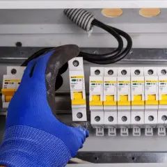 Ręka w niebieskiej rękawicy montuje bezpiecznik w skrzynce. Elektryk zabezpiecza instalację przed przepięciem.