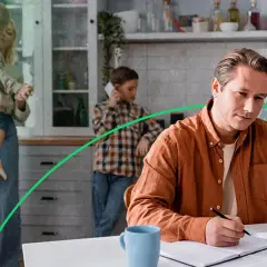 Mężczyzna w pomarańczowej koszuli pracuje przy laptopie, podczas gdy rodzina w tle cieszy się wspólnym czasem. Orange prąd w domu.