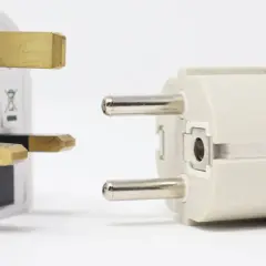 Adapter do gniazdek w Hiszpanii. Biały adapter z bolcami brytyjskimi obok jasnoszarego z bolcami europejskimi.