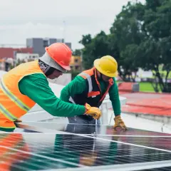 Dwóch pracowników z **świadectwem kwalifikacyjnym e** montuje panele słoneczne na dachu.