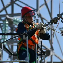 Elektryk w kasku i kamizelce pracujący na wysokości. Ciekawe, ile zarabia elektryk za taką odpowiedzialną pracę.