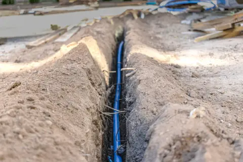 Niebieski kabel w wykopie, zabezpieczony w peszlu, czeka na zasypanie.