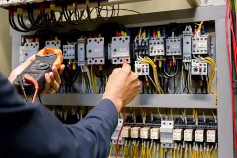 Ręce elektryka z multimetrem przy panelu sterowania. Przygotowanie do egzaminu SEP: pytania i odpowiedzi.