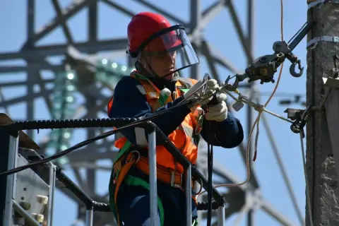 Elektryk w kasku i kamizelce pracujący na wysokości. Ciekawe, ile zarabia elektryk za taką odpowiedzialną pracę.