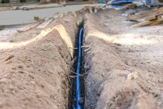 Niebieski kabel w wykopie, zabezpieczony w peszlu, czeka na zasypanie.