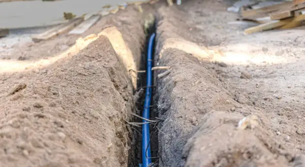 Niebieski kabel w wykopie, zabezpieczony w peszlu, czeka na zasypanie.