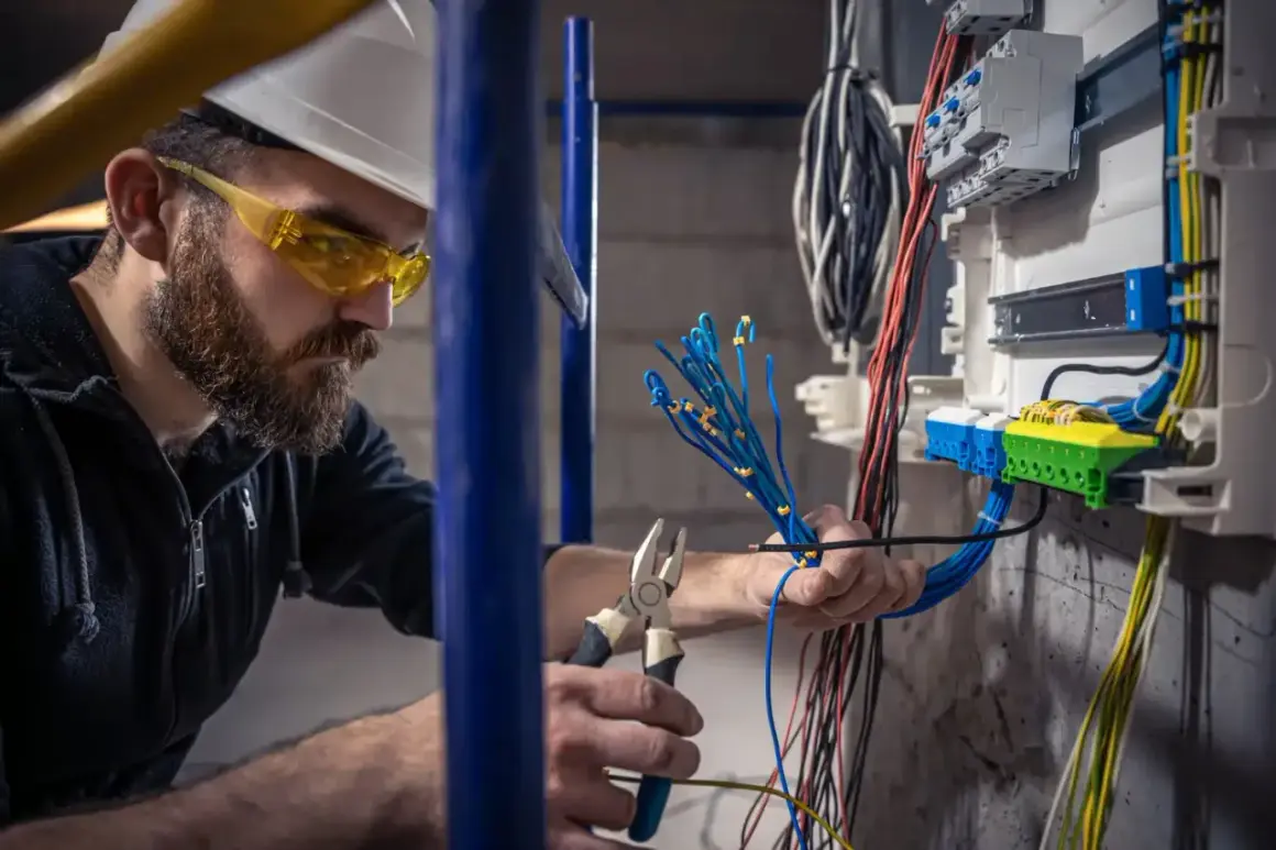 Elektryk z uprawnieniami budowlanymi elektrycznymi pracuje przy instalacji, przygotowując przewody do podłączenia w skrzynce rozdzielczej.