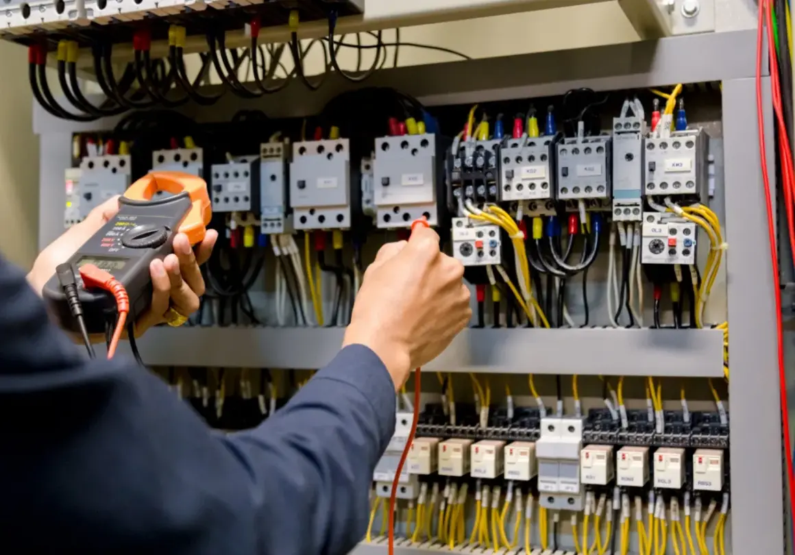 Ręce elektryka z multimetrem przy panelu sterowania. Przygotowanie do egzaminu SEP: pytania i odpowiedzi.