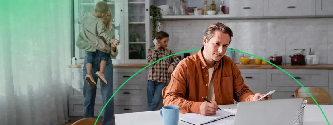 Mężczyzna w pomarańczowej koszuli pracuje przy laptopie, podczas gdy rodzina w tle cieszy się wspólnym czasem. Orange prąd w domu.