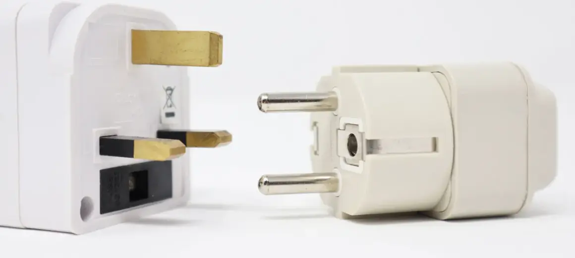 Adapter do gniazdek w Hiszpanii. Biały adapter z bolcami brytyjskimi obok jasnoszarego z bolcami europejskimi.
