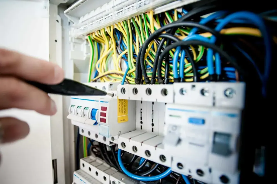 Ręka majstruje przy skrzynce z bezpiecznikami. Zastanawiasz się, ile zarabia elektryk w Niemczech?