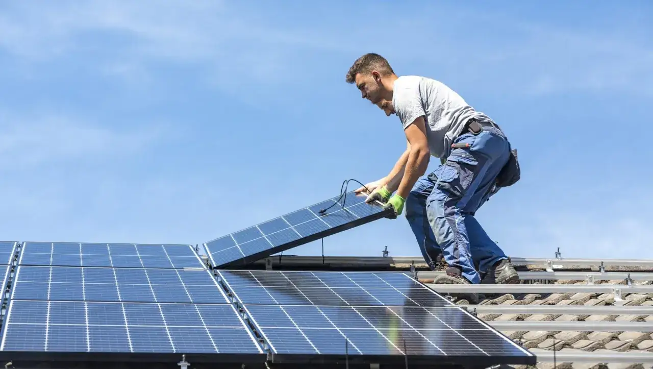 Elektryk montuje panele słoneczne na dachu. Zastanawiasz się, ile zarabia elektryk w Niemczech?