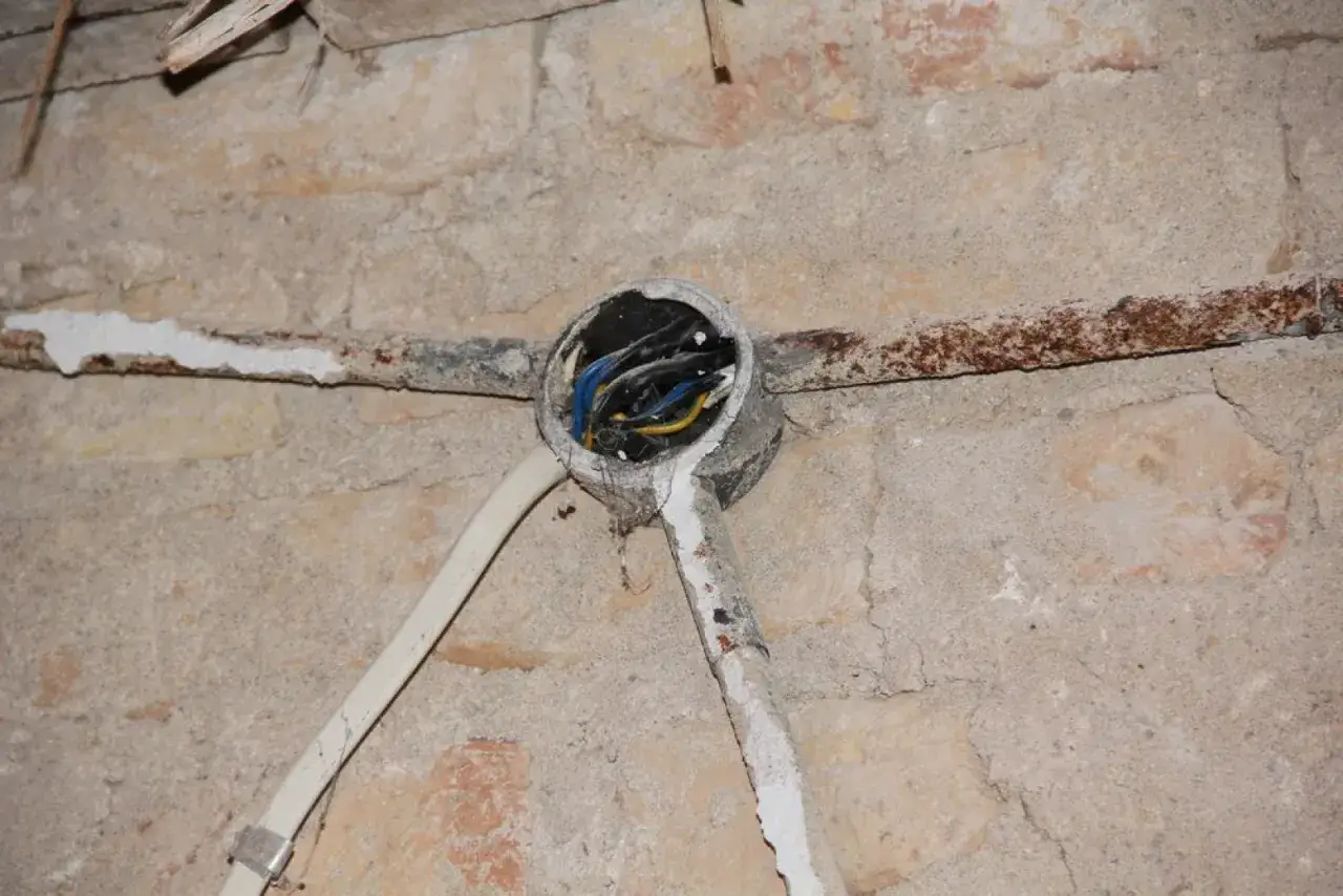 Otwarta puszka instalacyjna z przewodami, rdzewiejąca rura nad nią. Widać fragmenty starej instalacji, co może być punktem wyjścia do rozważań, jak zrobić uziemienie w starej instalacji.