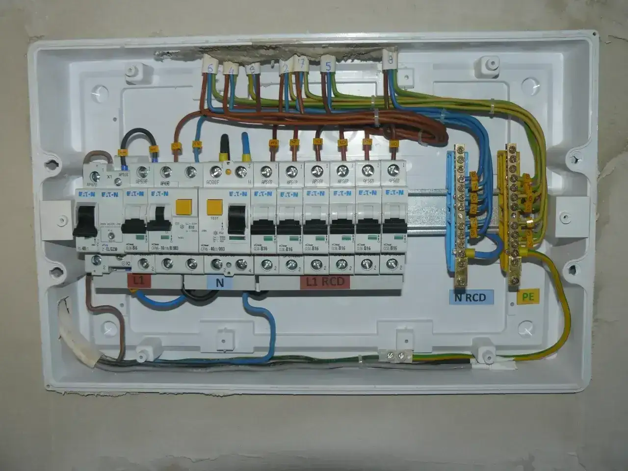 Instalacja elektryczna z bezpiecznikami. Zasilanie bezpiecznika z góry czy z dołu? Widać przewody fazowe, neutralne i ochronne.