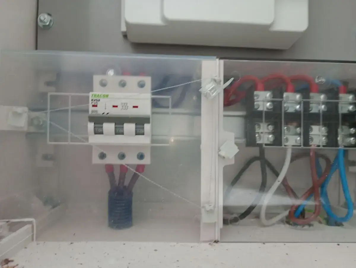 Wnętrze skrzynki elektrycznej z widocznym zabezpieczeniem przedlicznikowym, wyłącznikiem i przewodami.