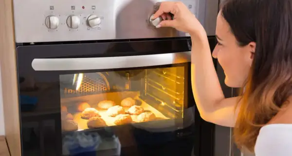 Kobieta ustawia temperaturę piekarnika, zastanawiając się, ile prądu zużywa piekarnik podczas pieczenia ciasteczek.