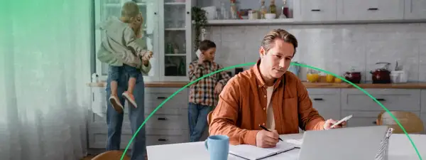 Mężczyzna w pomarańczowej koszuli pracuje przy laptopie, podczas gdy rodzina w tle cieszy się wspólnym czasem. Orange prąd w domu.