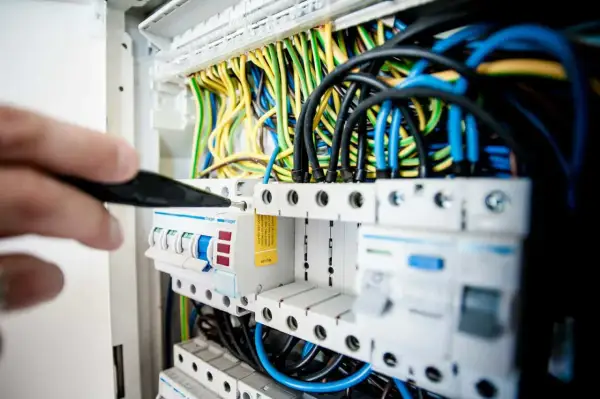 Ręka majstruje przy skrzynce z bezpiecznikami. Zastanawiasz się, ile zarabia elektryk w Niemczech?